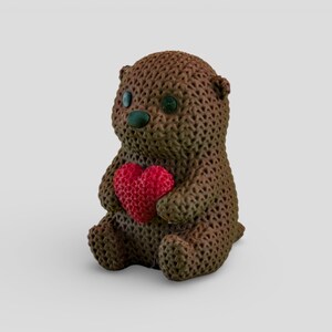 A brown knitted teddy bear holding a red heart-shaped object.