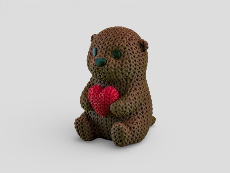 A brown knitted teddy bear holding a red heart-shaped object.