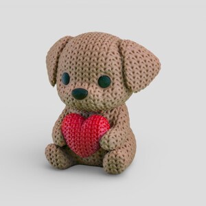 A brown crocheted teddy bear holding a red heart-shaped object.