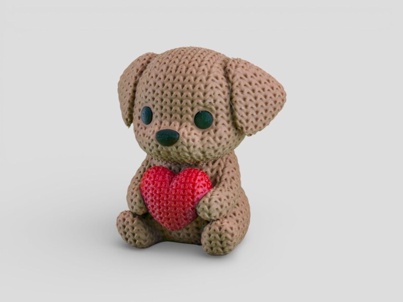 A brown crocheted teddy bear holding a red heart-shaped object.