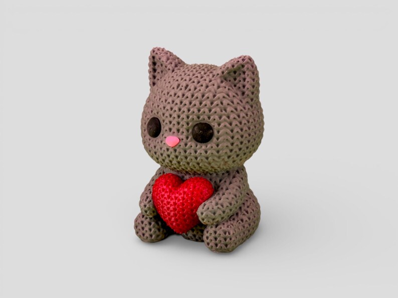 A small, brown, knitted stuffed animal cat holding a red heart.