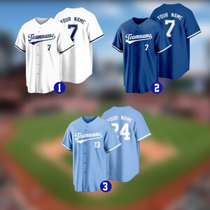 May include: Three baseball jerseys in white, blue, and light blue. Each jersey features a team name, number, and space for a personalized name on the back. The jerseys have button-up fronts and contrasting trim.