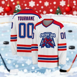 May include: White hockey jersey with red and blue accents. The jersey features the text "YOURNAME" and the number "00" on the back. The front displays a logo with the text "CUSTOM LOGO" and a hockey goalie graphic. The sleeves have red and blue stripes.