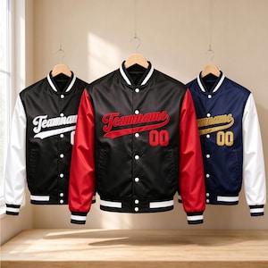 May include: Three varsity jackets hanging on wooden hangers. The left jacket is black with white sleeves, the center is black with red sleeves, and the right is navy with white sleeves. Each features the text Teamname and the number 00.