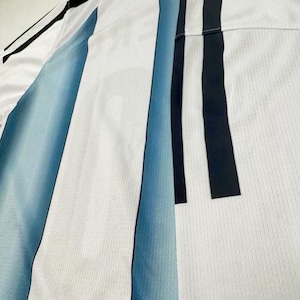 May include: White athletic jersey with blue and black vertical stripes. The jersey has a crew neck and a mesh-like texture. The stripes are a gradient of blue, fading from a darker shade to a lighter one.