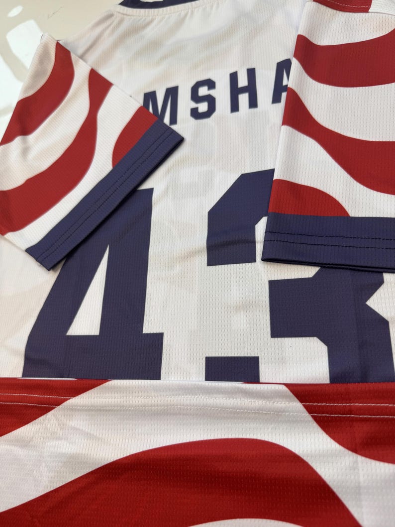 May include: White jersey with red and blue striped sleeves and accents. The number 43 is prominently displayed in navy blue, along with the name "MSHA" across the shoulders. The jersey has a mesh texture.