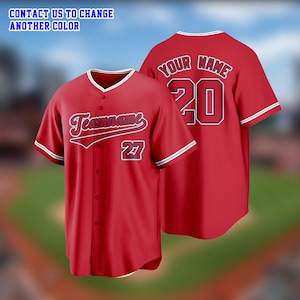 Peut inclure: Maillot de baseball rouge avec bordure blanche sur les manches et le col. Le devant porte le mot "Teamname" en écriture cursive et le numéro 27. Le dos affiche "YOUR NAME" au-dessus du numéro 20.