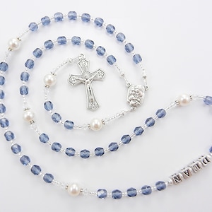 May include: A blue and white rosary with a silver cross and a silver charm with the word "DREAM" on it.