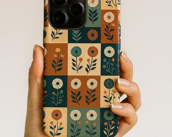 Puede incluir: Una funda de teléfono con un estampado floral. El diseño presenta una cuadrícula de cuadrados con flores en naranja, azul y blanco sobre un fondo marrón, verde y beige. La funda se sostiene en una mano.