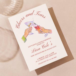 Op de afbeelding: Een witte kaart met rode tekst die "Cheers and Tears" en "Let's have a fond farewell toast to Lara Cole's new adventure in Ocean City!" luidt. De kaart bevat ook een afbeelding van twee handen die cocktailglazen omhoog houden.