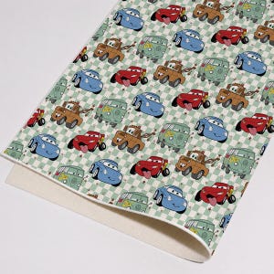 May include: A sheet of patterned material featuring a repeating print of cartoon characters from the movie Cars, including red race cars, blue sports cars, brown tow trucks, and green vans, set against a light green and white checkered background.