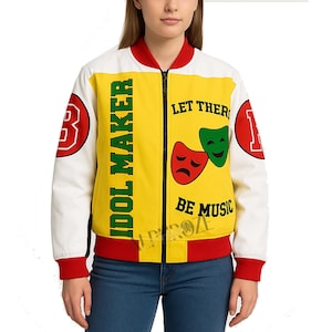 Puede incluir: Chaqueta bomber amarilla, blanca y roja con las palabras "IDOL MAKER" y "LET THER BE MUSIC" impresas. La chaqueta tiene cierre de cremallera y detalles en rojo y blanco. Las mangas son blancas con parches rojos.