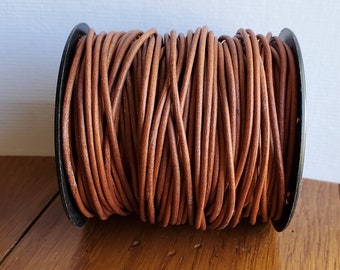 May include: A spool of brown leather cord wound around a black plastic bobbin. The cord is approximately 1/4 inch thick.