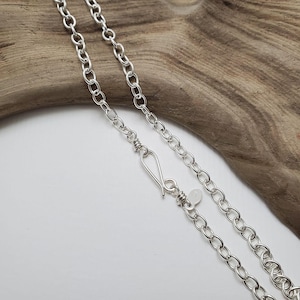 May include: A silver chain necklace with a lobster clasp closure. The chain is made of small, oval-shaped links.