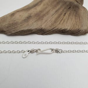 May include: A silver chain necklace with a lobster clasp closure. The chain is made of small, round links. The tag on the chain reads "925".