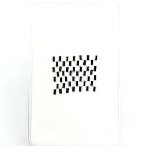 May include: A collection of small, rectangular black gemstones arranged in a grid pattern on a white surface. Each individual stone features a smooth, flat surface and sharp, defined edges, creating a uniform appearance across the entire set.
