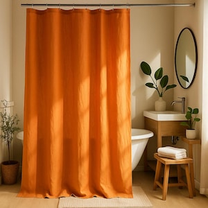 May include: An orange shower curtain hangs in a bathroom. The curtain is made of a textured fabric and is the focal point of the room. A white bathtub, wooden vanity, and oval mirror are also visible.
