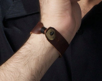 May include: A brown leather bracelet with a metal clasp and a black cord detail.