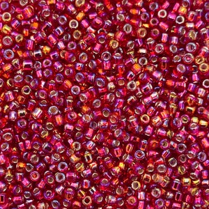 May include: A close-up image of a large quantity of small, red, iridescent glass beads. The beads are round and have a metallic sheen.