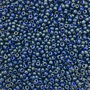May include: A close-up view of a large quantity of dark blue seed beads. The beads have a metallic sheen and are arranged in a random pattern.