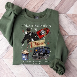 May include: Green sweatshirt with a graphic featuring elements from "The Polar Express." The design includes a conductor's uniform, a red gift bag, a train, and a mug of cocoa. Text includes "Polar Express" and "Believe."