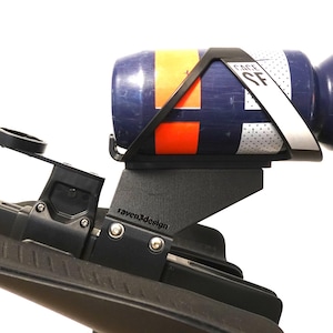 May include: Black bicycle accessory with a water bottle holder. The holder is mounted on a black bracket and holds a blue water bottle with orange and white accents. The bottle has a white strap with "FACE SF" printed on it.