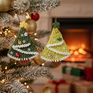 Könnte beinhalten: Zwei handgefertigte Weihnachtsbaum-Ornamente aus Häkelarbeit in Form von Tannenbäumen. Eines ist grün mit weißen Akzenten, das andere hellgrün. Beide haben dekorative Elemente wie Schneeflocken und kleine Figuren.
