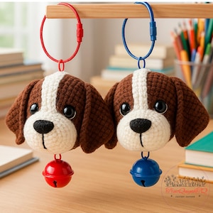 Può includere: Due portachiavi a forma di cane fatti a mano all'uncinetto. Ogni portachiavi presenta una testa di cane marrone e bianca con occhi neri e una campana rossa o blu. I portachiavi sono appesi a una barra di legno.