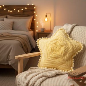 May include: A yellow star-shaped cushion with a textured pattern and a pom-pom trim sits on a cream blanket over a wooden chair. The cushion is the main focus, with a bedroom setting in the background.