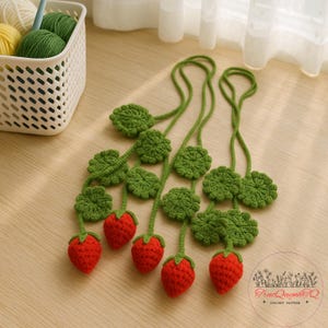 May include: Crocheted strawberry garland with red berries, green stems, and leaves. The handmade garland is designed with a repeating pattern of strawberries and leaves, perfect for home decor or crafting projects.