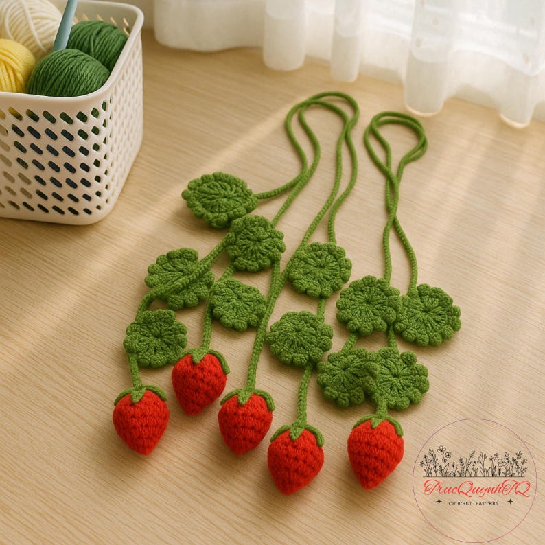 May include: Crocheted strawberry garland with red berries, green stems, and leaves. The handmade garland is designed with a repeating pattern of strawberries and leaves, perfect for home decor or crafting projects.