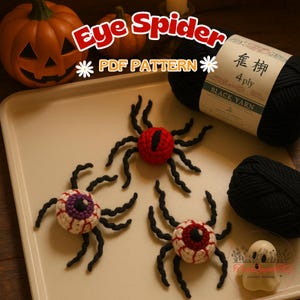 以下が含まれることがあります： ハロウィーンをテーマにした画像。黒い脚と赤、白、紫の目のディテールを持つ、3匹のかぎ針編みの目のクモ。クモはカボチャと黒い糸玉が入ったトレイの上にあります。「Eye Spider PDF Pattern」と書かれたテキスト。