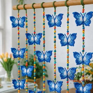 May include: A decorative hanging curtain featuring blue crochet butterflies with white accents. The butterflies are strung on colorful beaded strands, suspended from a wooden rod. The curtain adds a whimsical touch to any room.