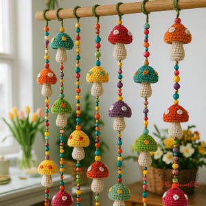 Puede incluir: Una colorida guirnalda de setas hecha a mano. Las setas de ganchillo presentan varios colores, incluyendo rojo, naranja, amarillo, verde y morado, con lunares blancos. Cada seta cuelga de una barra de madera con una cadena de cuentas de colores.