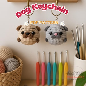 May include: Two crochet dog keyrings, one tan and one grey, suspended from gold rings. The keyrings are round with small ears and a pug-like face. The text "Dog Keychain PDF Pattern" is above the keyrings. Crochet hooks and yarn are in the background.
