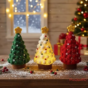 Puede incluir: Tres árboles de Navidad de ganchillo hechos a mano en verde, blanco y rojo, cada uno coronado con una estrella amarilla. Los árboles están iluminados, con un brillo cálido que emana desde adentro. Se encuentran sobre una superficie de madera, decorada con nieve artificial y bayas.