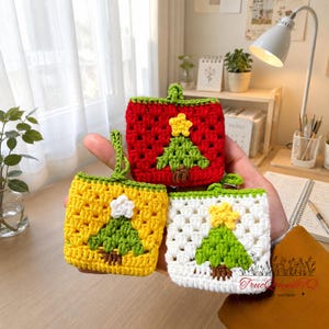May include: Three crocheted Christmas tree pouches in red, yellow, and white. Each pouch features a green tree with a yellow star and a brown trunk. The pouches are square-shaped with a loop for hanging.