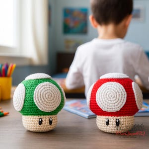 May include: Two crocheted mushroom figures, one green and one red, with white accents and smiling faces. The mushrooms are on a wooden surface, with a child in the background. The mushrooms are approximately 4 inches tall.
