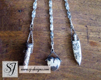 May include: A silver chain with three decorative pendants. The top pendant is a heart-shaped design with intricate details. The middle pendant is a heart-shaped locket. The bottom pendant is a long, pointed bottle with a floral design. The chain is hanging from a decorative silver clasp.