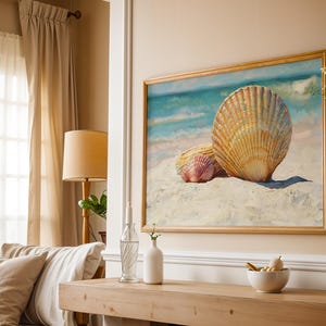 May include: A framed painting depicts three seashells on a sandy beach with a blue ocean backdrop. The large shell is tan and orange, with a smaller pink shell beside it. The artwork is displayed in a room with neutral tones.