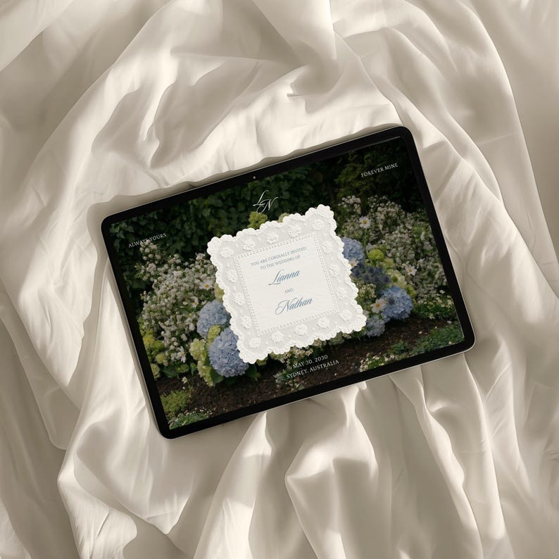 May include: A digital tablet displaying a wedding invitation with a white scalloped border over a background of blue and white hydrangeas. The text reads: You are cordially invited to the wedding of Lianna and Nathan, May 30, 2030, Sydney, Australia.