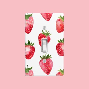 May include: White light switch cover with a pattern of red watercolour strawberries. The switch is labelled "OFF".