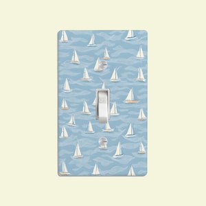 May include: A light blue light switch cover with a white light switch and a pattern of white sailboats on a blue background.