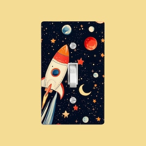 May include: A light switch cover with a rocket ship flying through space. The background is a dark blue with white stars, planets, and a crescent moon. The switch is labeled "OFF".