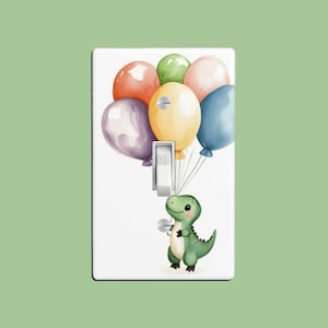 May include: A light switch cover featuring a green dinosaur holding a bunch of colourful balloons. The balloons are red, yellow, green, blue and purple. The switch is labelled "OFF".