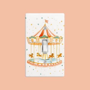 May include: A white light switch cover with a watercolor illustration of a carousel with horses and a red and white striped canopy. The background is white with green and gold stars.