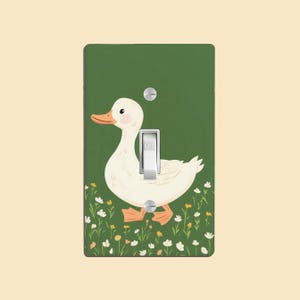 May include: A green light switch cover featuring a white duck illustration and a light green field of flowers. The switch is labelled "OFF".