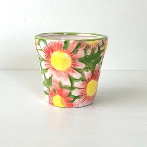 以下が含まれることがあります： 花柄の陶器鉢。ピンクと赤の花に黄色の中心と緑の葉の模様が特徴です。縁は緑色で、内側は薄いピンク色です。