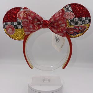 Può includere: Fascia per capelli con orecchie di Minnie Mouse rosse e dorate a tema Cars. Le orecchie sono impreziosite da glitter rossi e strass. Il fiocco presenta una stampa Cars. La fascia è rossa con finiture dorate. Le orecchie hanno il logo Cars e Saetta McQueen.
