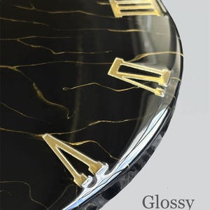 May include: Close-up of a black clock face with gold Roman numerals and gold veining. The clock has a glossy finish, with the words "Glossy Finish" in the lower right corner.